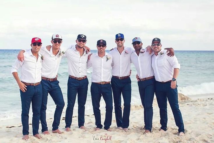 a group of men standing next to each other on top of a sandy beach near the ocean