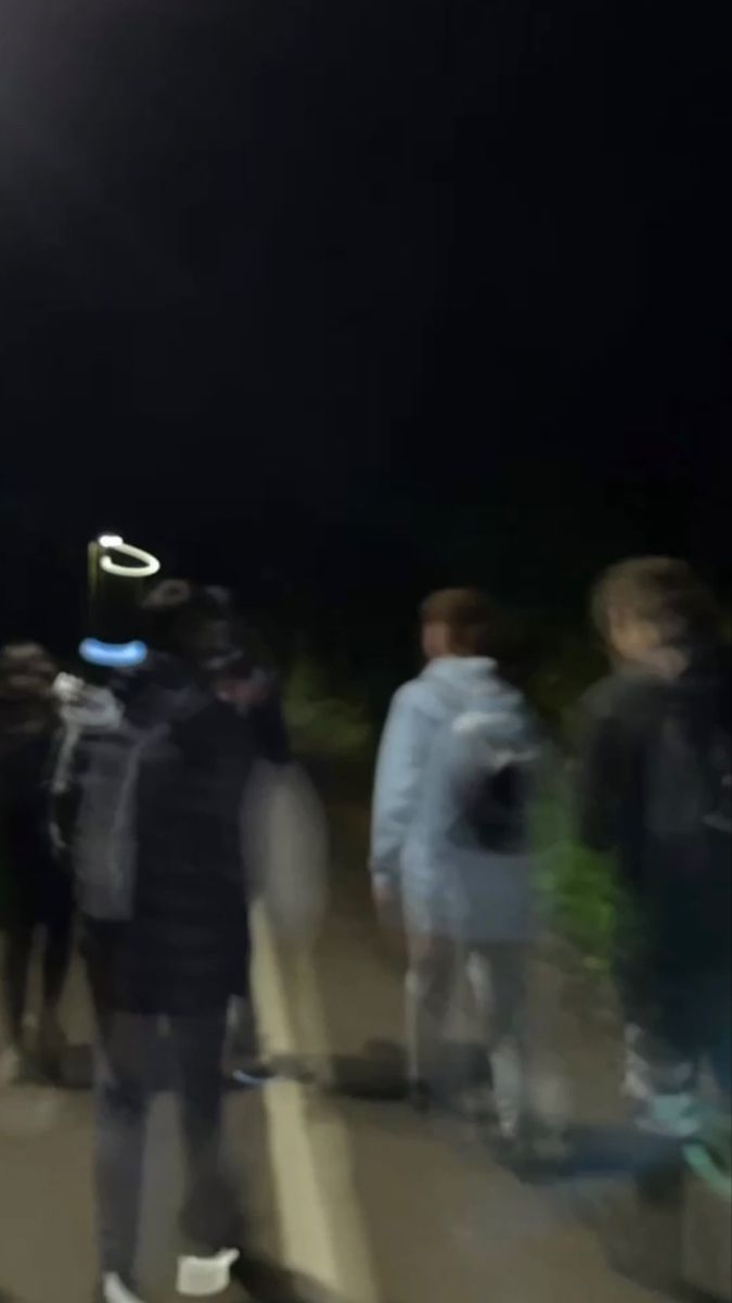 a group of people standing on the side of a road under a street light at night