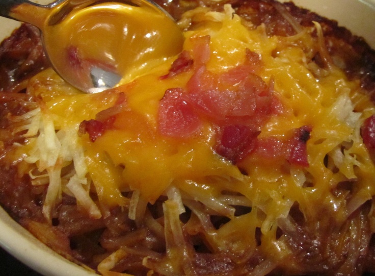 a white bowl filled with chili and cheese covered casserole next to a spoon