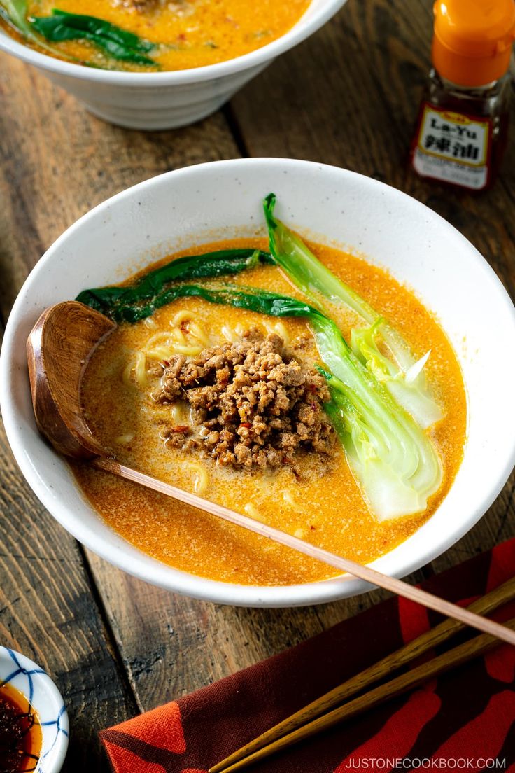 two bowls of soup with chopsticks on a table next to some other dishes