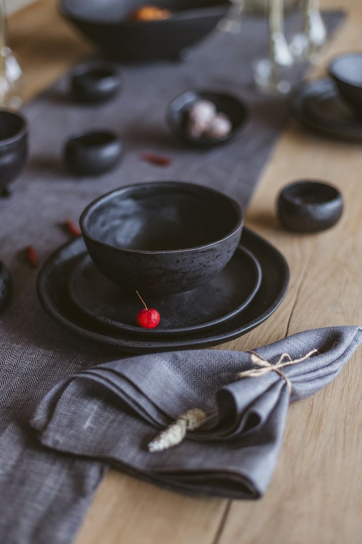 a table topped with black plates and bowls on top of a wooden table covered in cloth