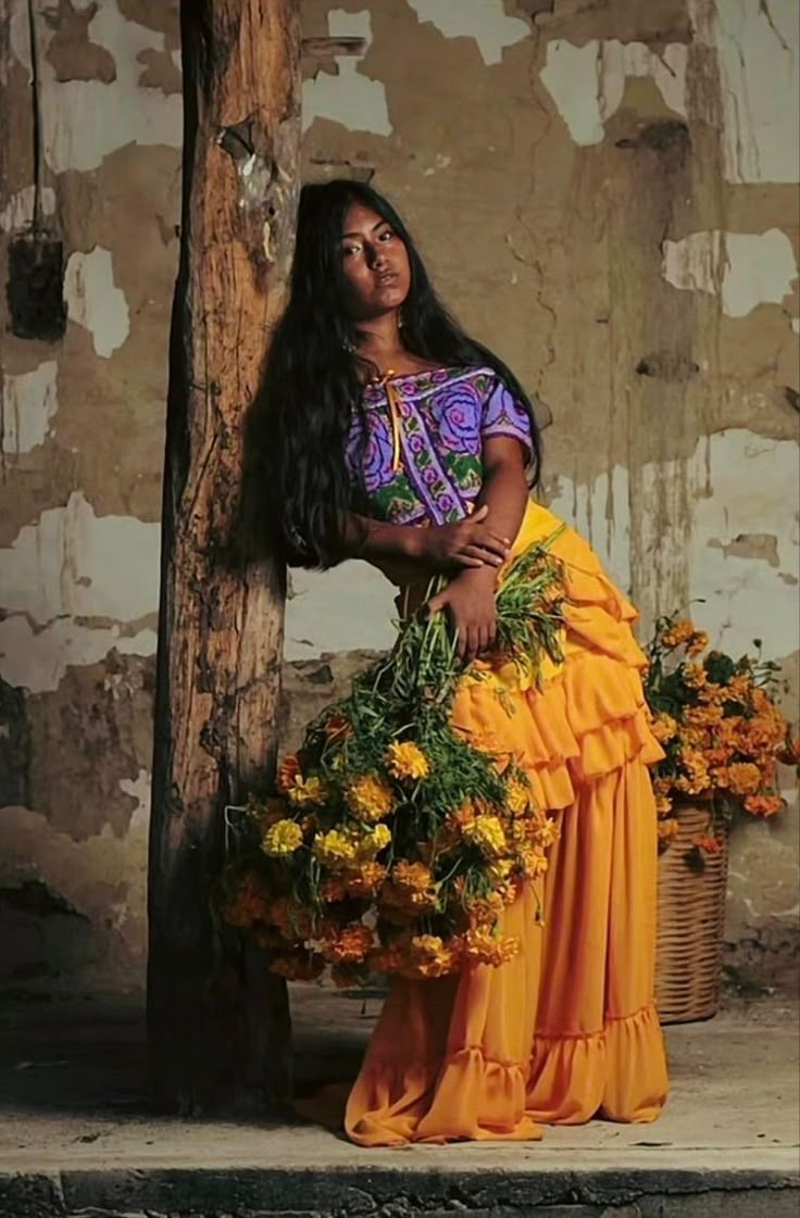 a woman with long black hair is sitting on a wooden pole holding yellow flowers in her hands