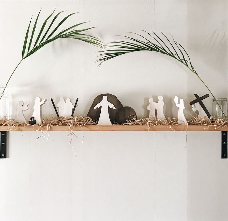 a shelf filled with figurines and plants on top of a white wall next to a palm tree