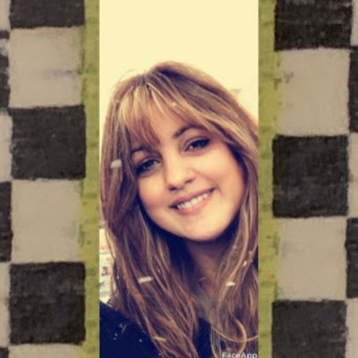 a woman with long hair is smiling and looking at the camera from behind a checkered wall