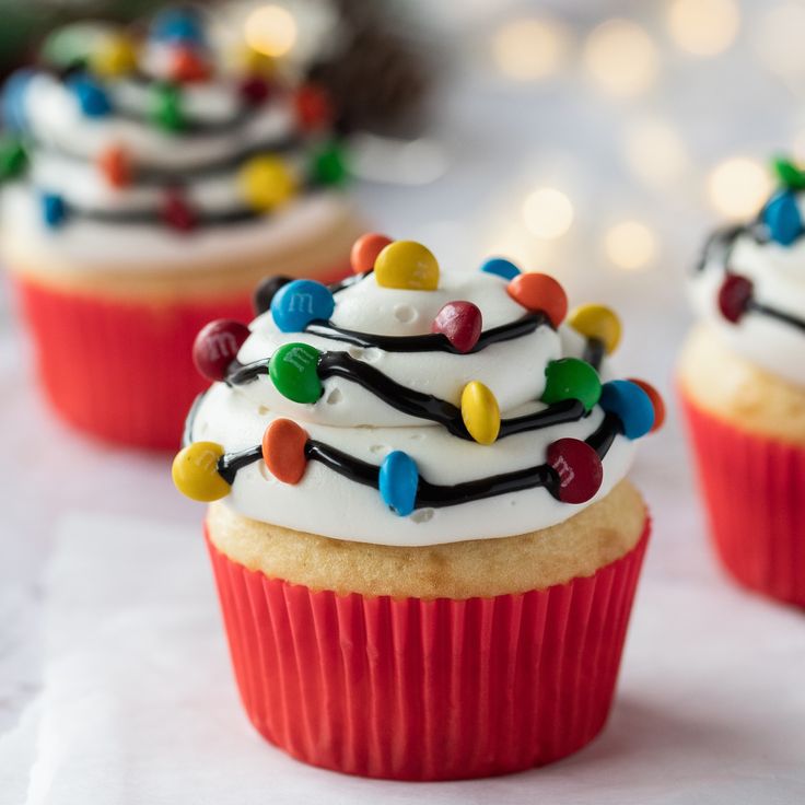 three cupcakes with white frosting and christmas lights on them