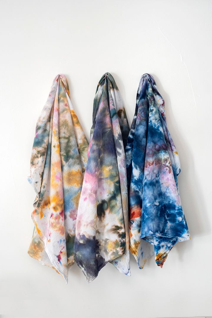 three scarves are hanging on the wall, one is multicolored and the other is blue