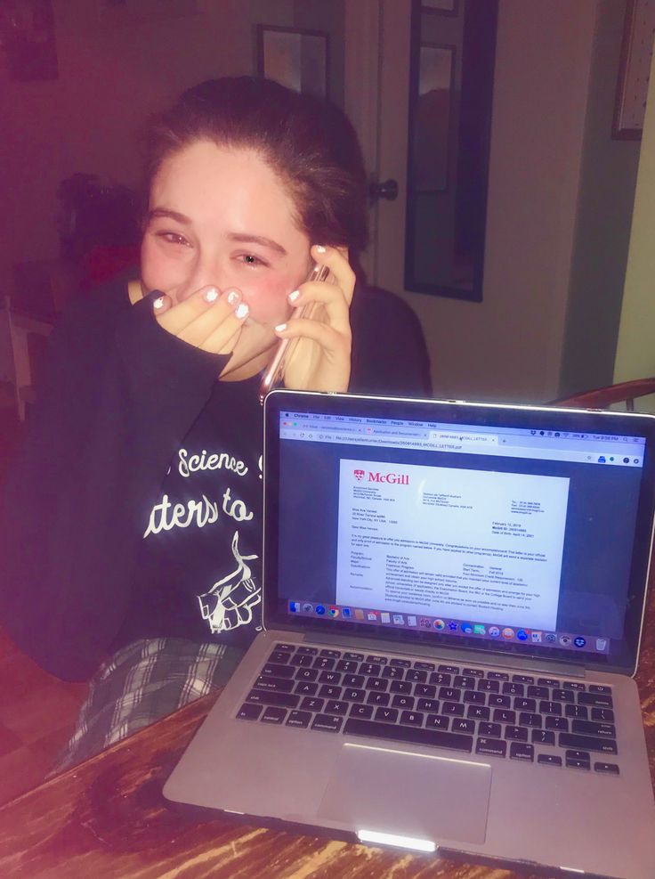 a girl covers her face with her hands as she sits in front of an open laptop computer