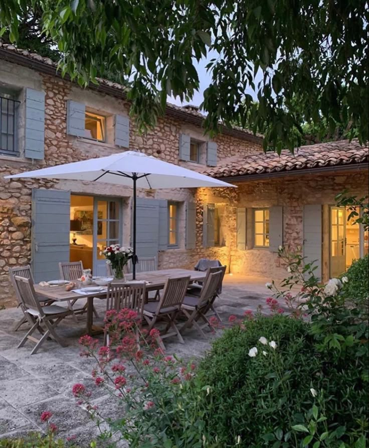 an outdoor dining area with table, chairs and umbrella in front of a stone building