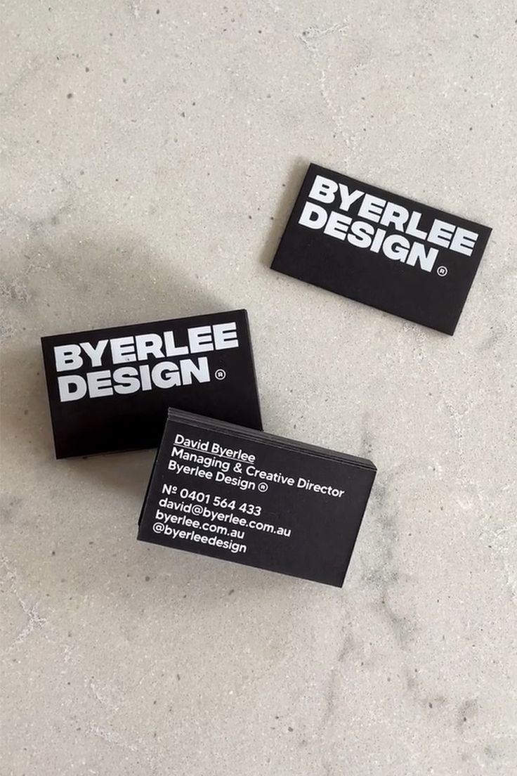 three black business cards sitting on top of a white counter next to an orange cell phone