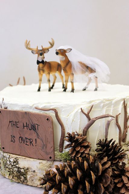 two deer figurines sitting on top of a white frosted cake with pine cones