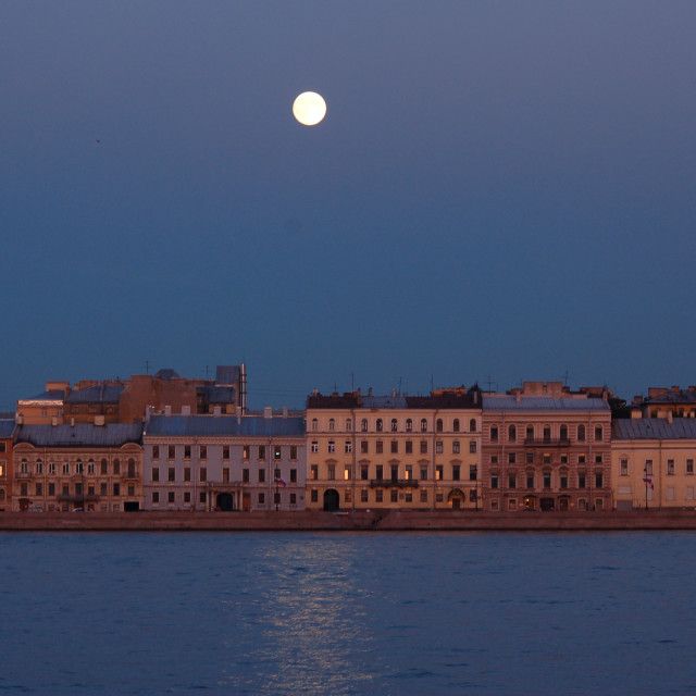 the moon is setting over some old buildings on the water's edge in front of it