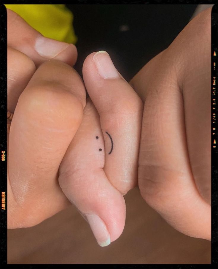 two hands holding each other with small tattoos on their thumb and fingernails in the middle