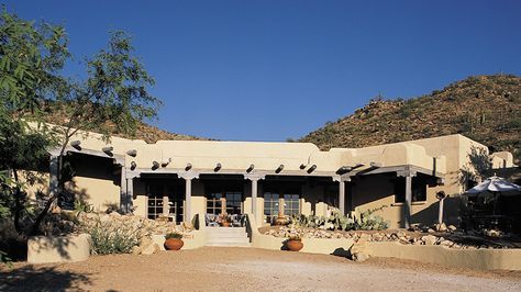 an adobe - style house in the desert surrounded by trees and rocks, with large courtyard