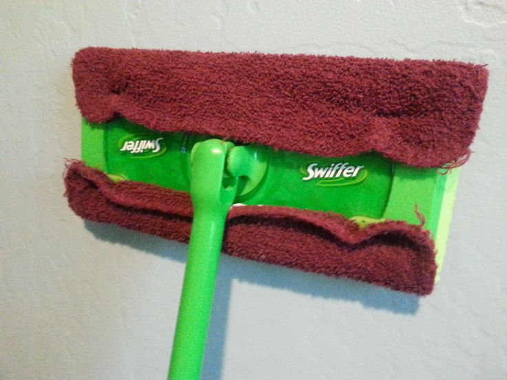 a green mop is hanging on the wall with a red towel and swiffer