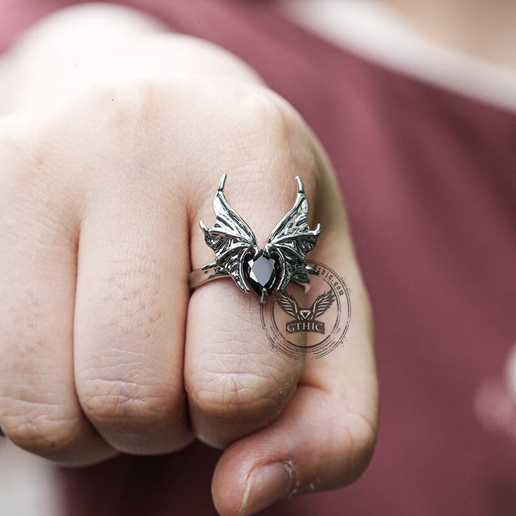 Embrace the darkness with our Dark Bat alloy adjustable ring. This unique accessory features a captivating bat design, crafted with meticulous attention to detail. Black Stainless Steel Rings For Halloween, Halloween Black Stainless Steel Ring, Gothic Winged Jewelry Gift, Gothic Winged Jewelry For Gifts, Black Fantasy Rings As Gift, Fantasy Style Black Ring For Gift, Black Fantasy Style Rings As Gift, Fantasy Rings For Halloween Gift, Adjustable Gothic Stainless Steel Rings