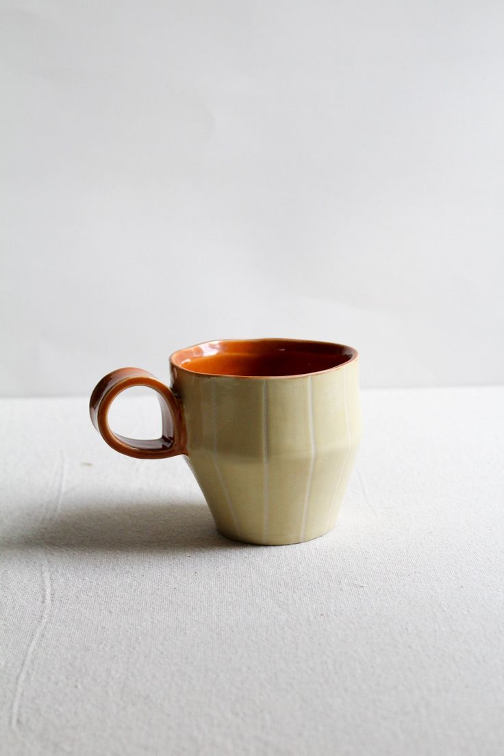 a white and brown cup sitting on top of a table next to a white wall