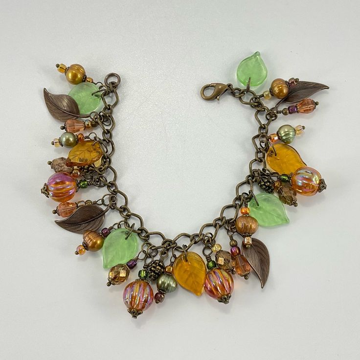 a multicolored necklace with leaves and beads on it's chain, sitting on a white surface