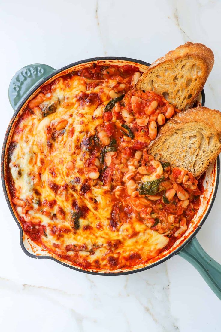 a casserole dish with bread and beans in it on a marble countertop