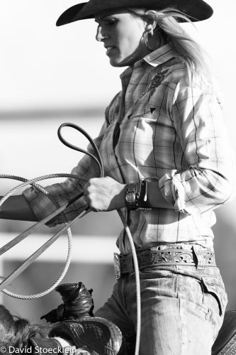 black and white photograph of a woman in cowboy attire holding a lasso while riding a horse