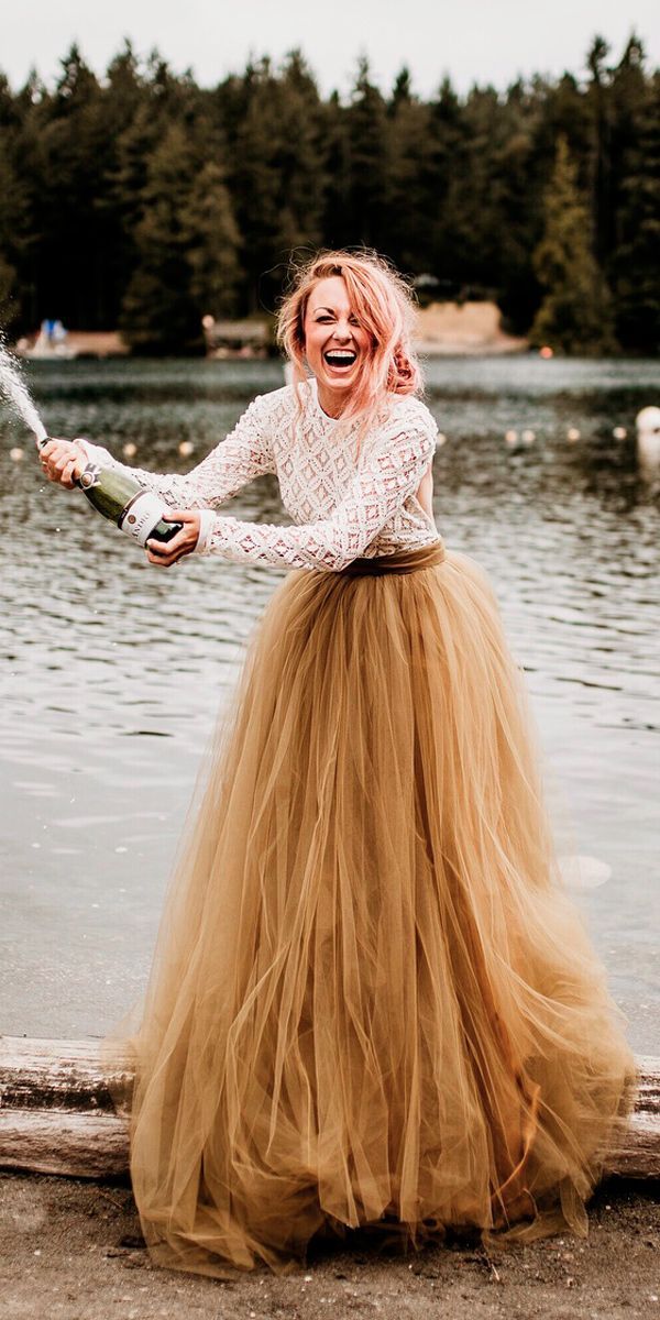 a woman in a long skirt is holding a bottle and standing on the shore of a lake