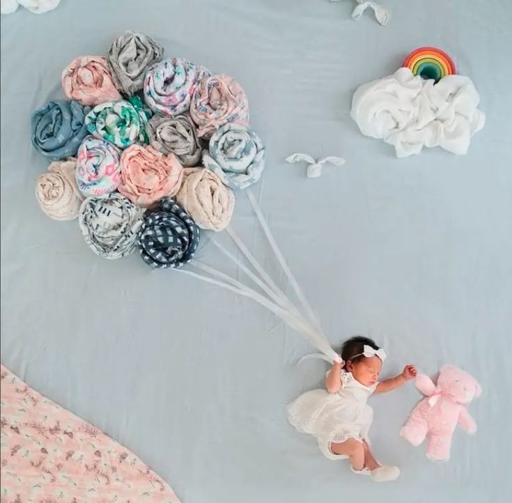 a baby girl holding onto a bunch of fabric flowers with a pink teddy bear next to it