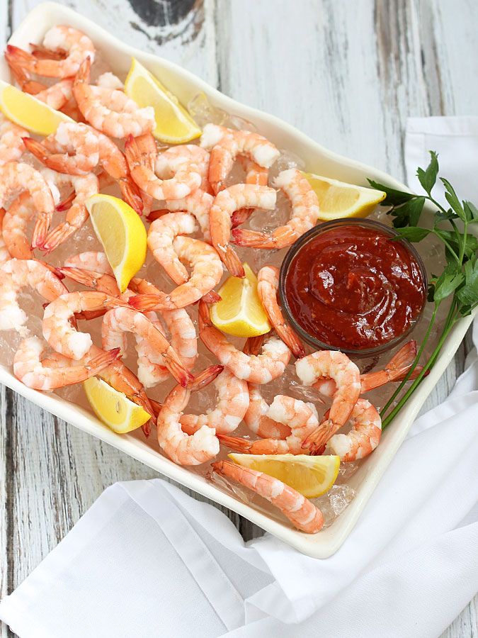 a white platter filled with shrimp and lemon wedges next to ketchup