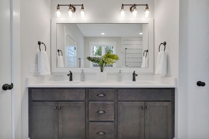 a bathroom with two sinks, mirrors and lights on the wall above them is shown