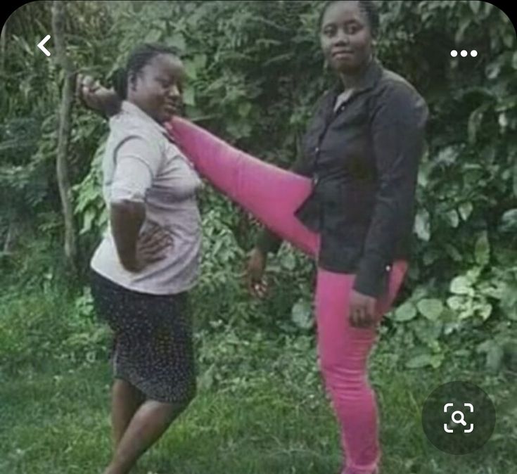 two women are standing in the grass and one is stretching her leg