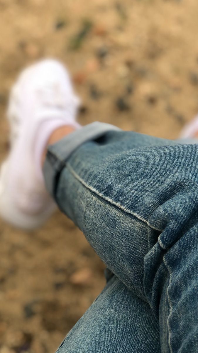 a person's legs with white shoes and blue jeans on the ground in front of them