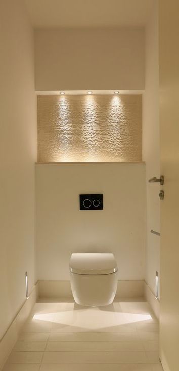 a white toilet sitting in the middle of a bathroom next to a wall mounted light