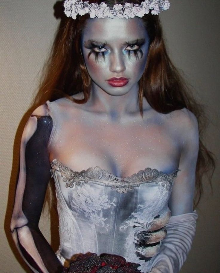 a woman with makeup and make - up is holding a cake in one hand and wearing gloves on the other