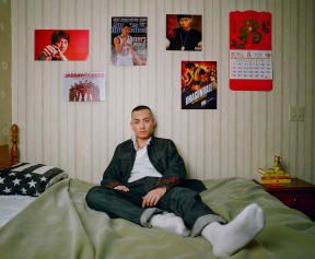 a man sitting on top of a bed next to a wall with posters hanging above it