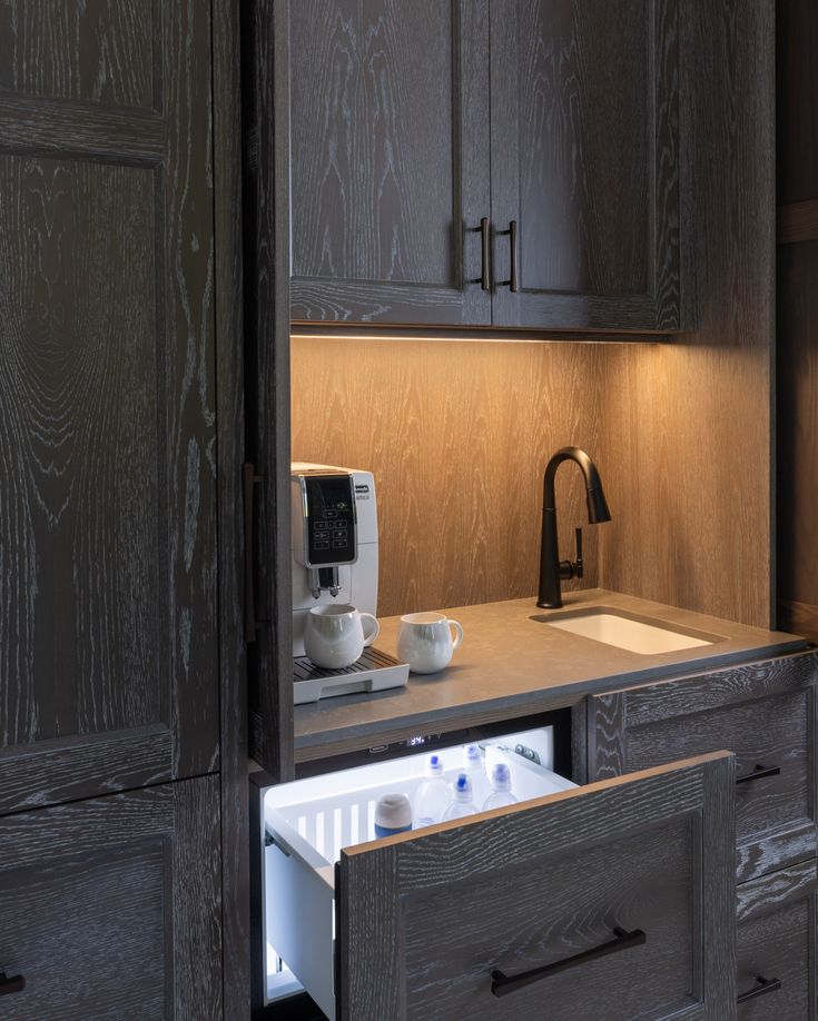 a kitchen with dark wood cabinets and white dishes on the counter top in front of a coffee maker