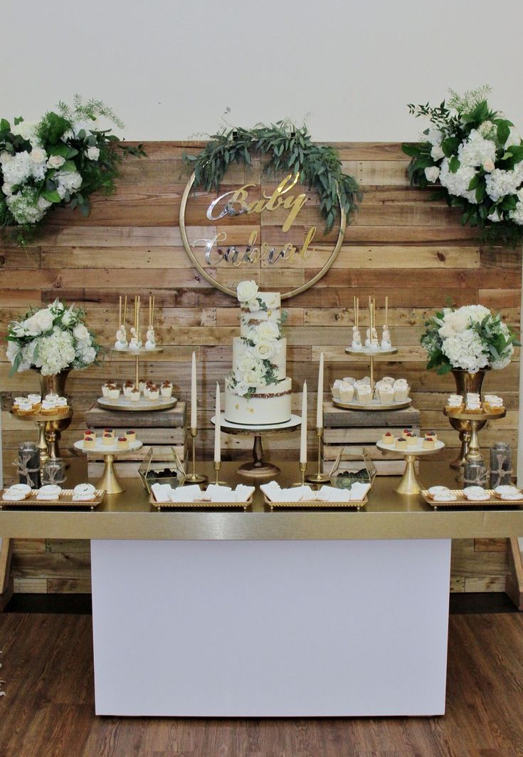 the dessert table is set up with white flowers and greenery on top of it