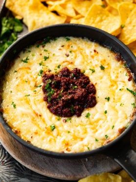 a bowl of cheese dip with tortilla chips on the side and salsa in it