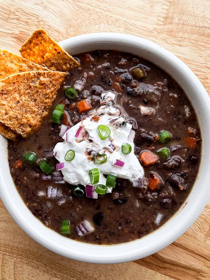 a bowl of black bean soup with sour cream and tortilla chips on the side