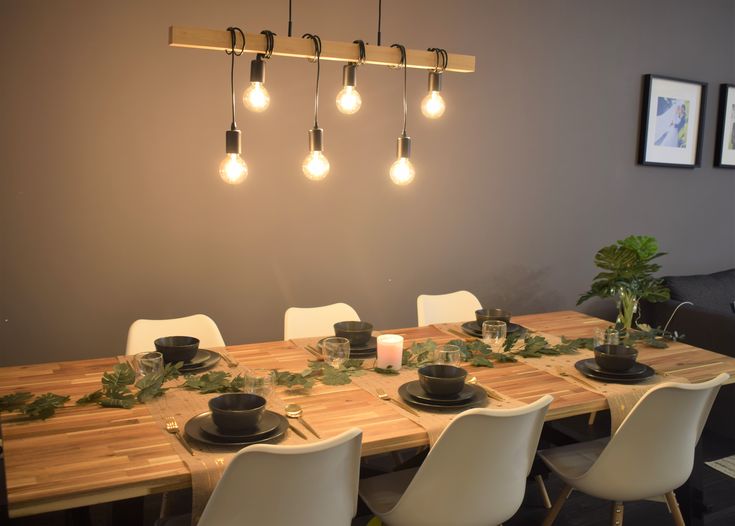 a wooden table with white chairs and lights hanging from it's ceiling in a dining room