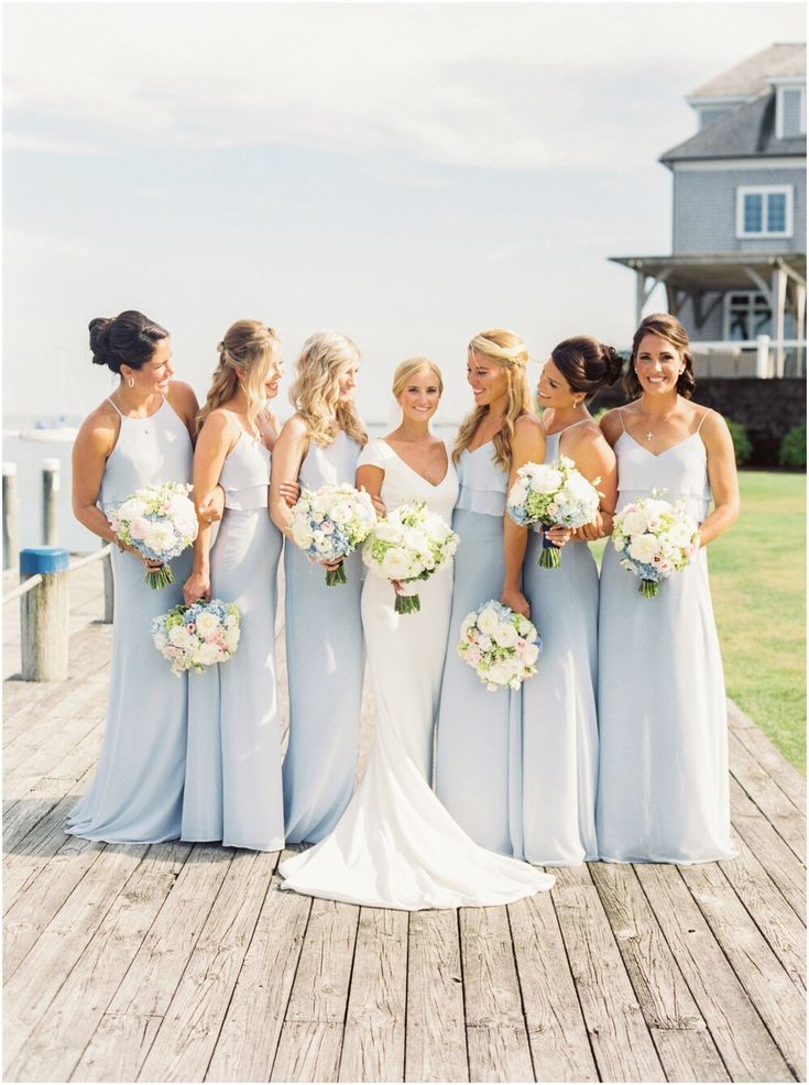 a group of women standing next to each other on a wooden pier holding bouquets