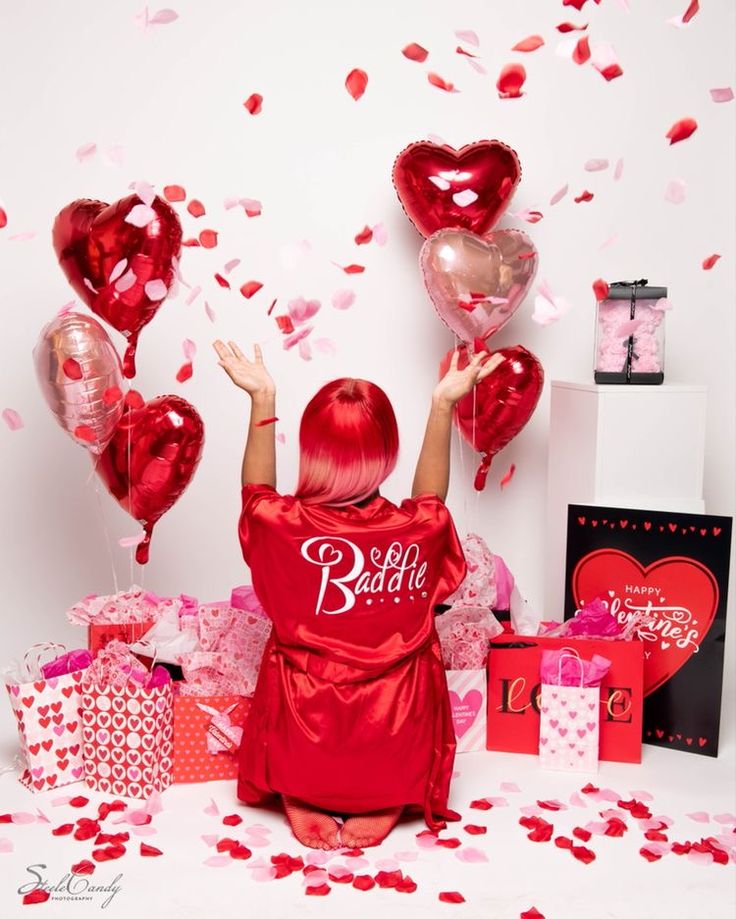 a woman with red hair sitting on the floor surrounded by balloons and confetti