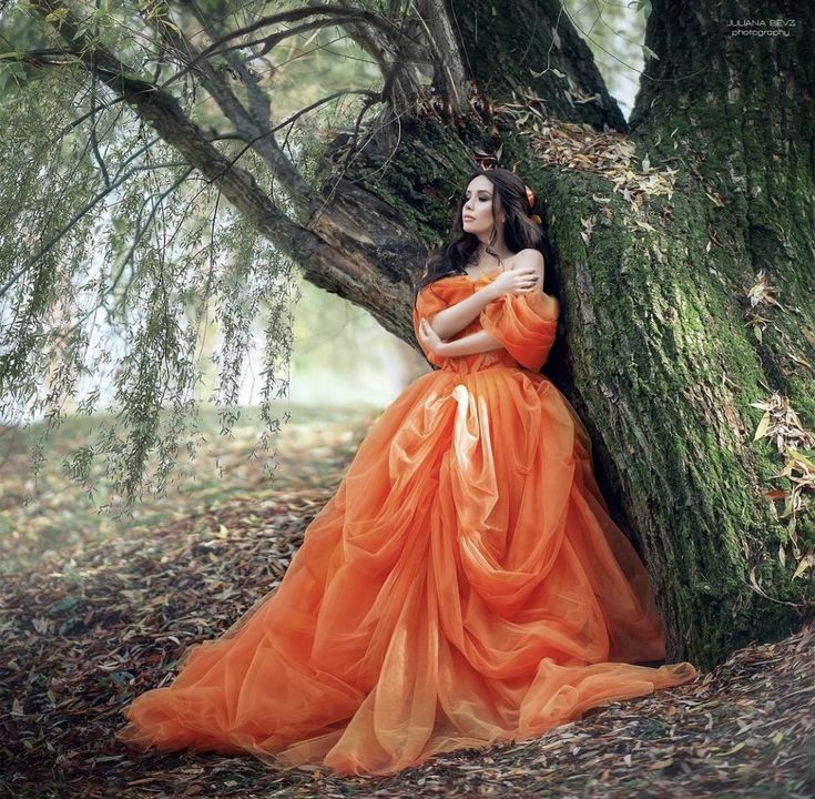 a woman in an orange dress leaning against a tree