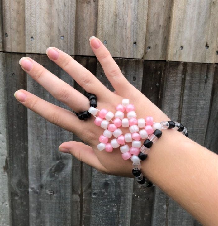 a woman's hand with pink and white beads on it, wearing a black beaded bracelet