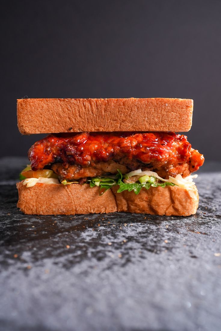 a sandwich with meat, lettuce and tomato sauce on a black surface in front of a dark background