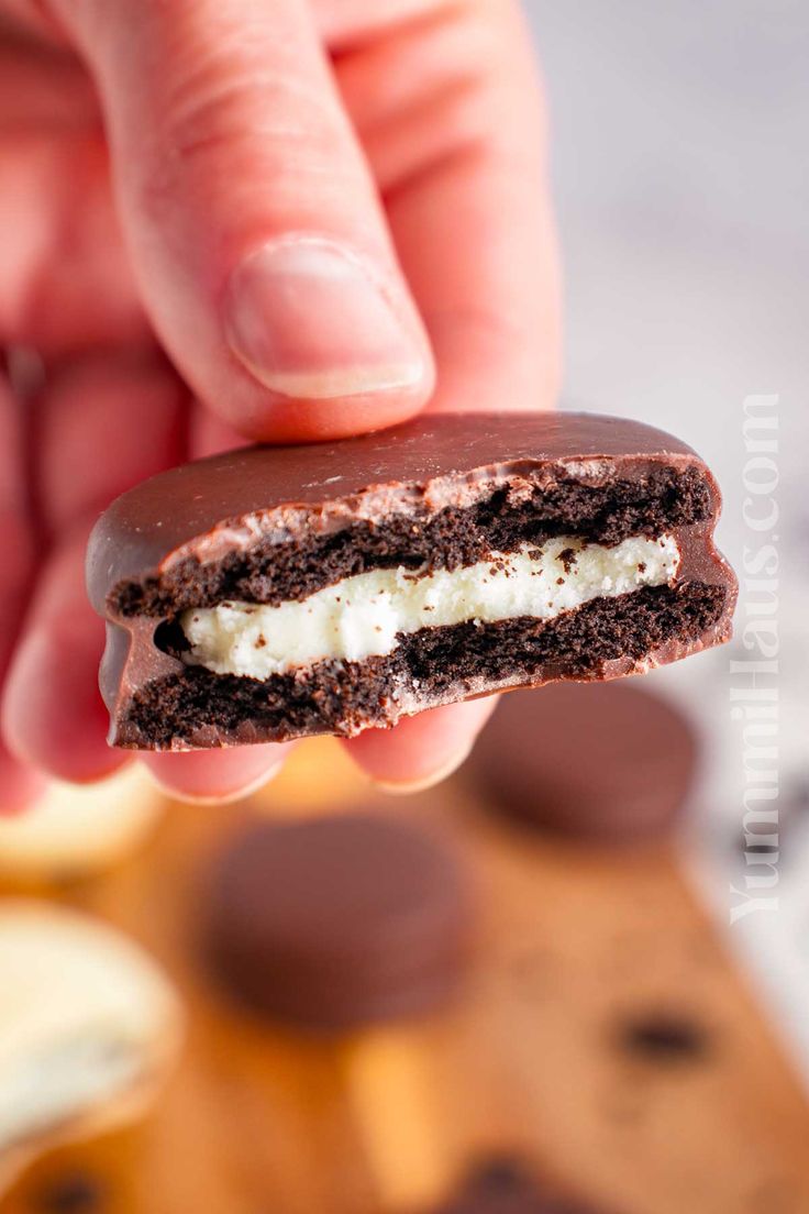 a hand holding a half eaten chocolate ice cream sandwich with white filling in it's center