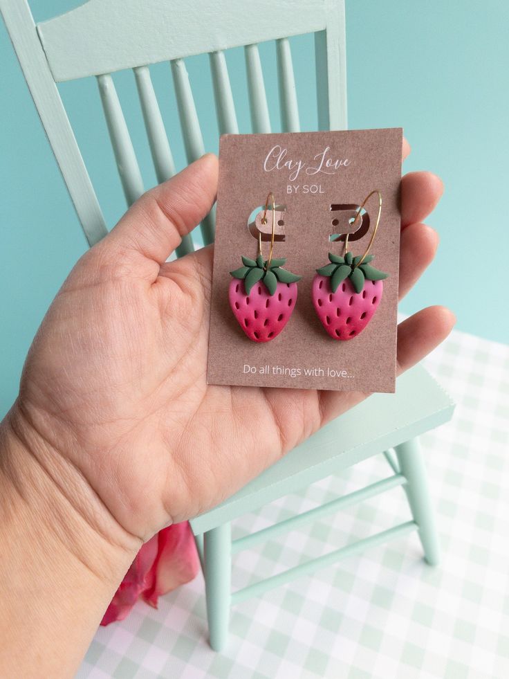 a person holding up a pair of strawberry earrings