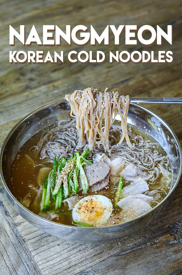 a bowl filled with noodles, meat and veggies on top of a wooden table