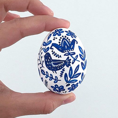 a hand holding an egg decorated with blue and white designs on it's side