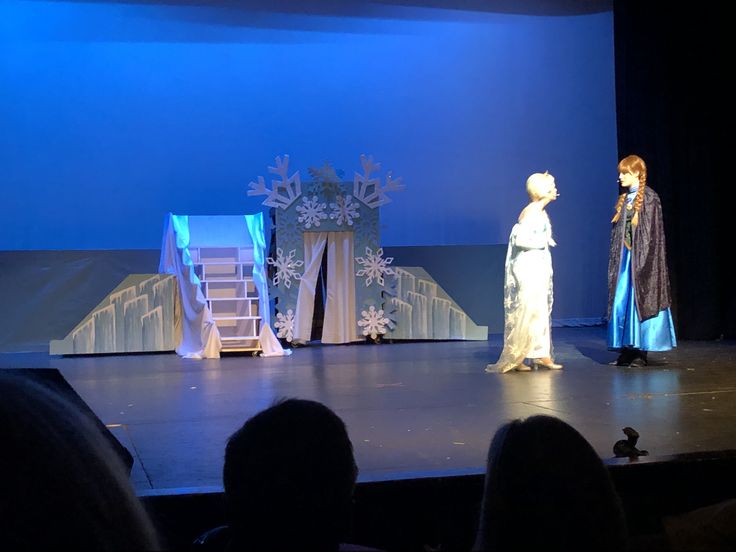 two women standing on a stage in front of a blue backdrop with snowflakes