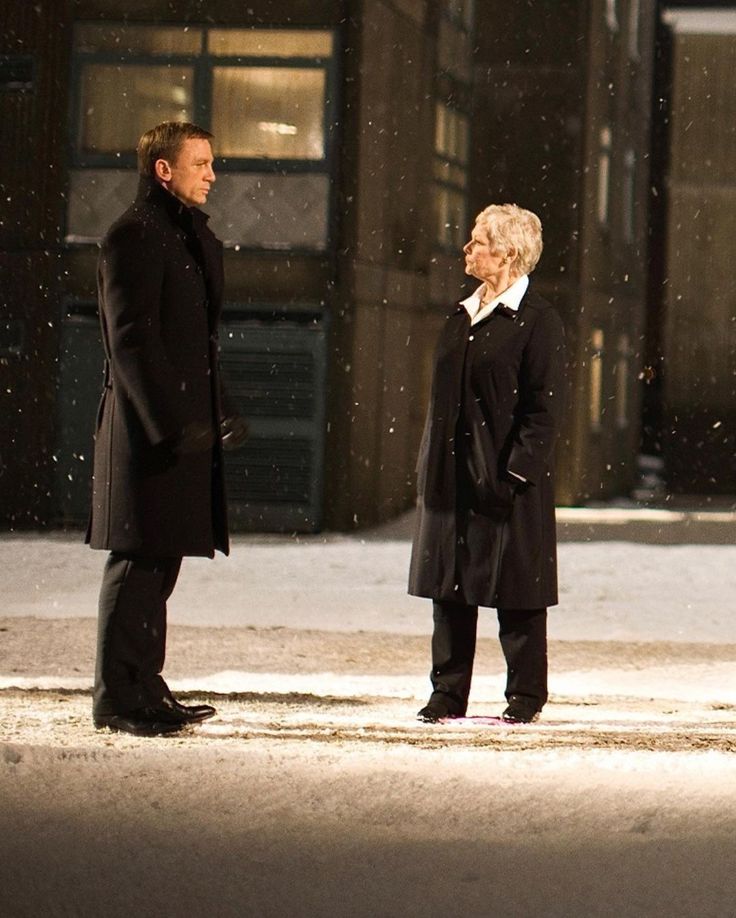 two people are standing in the snow talking to each other and one is wearing a black coat