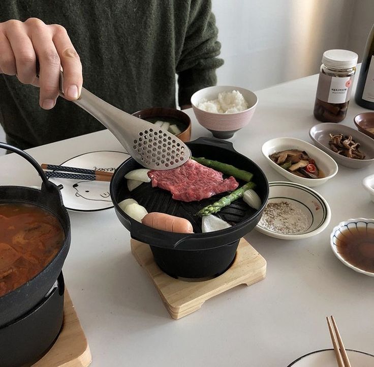 a person is cooking food in a pot on the table with other dishes around him