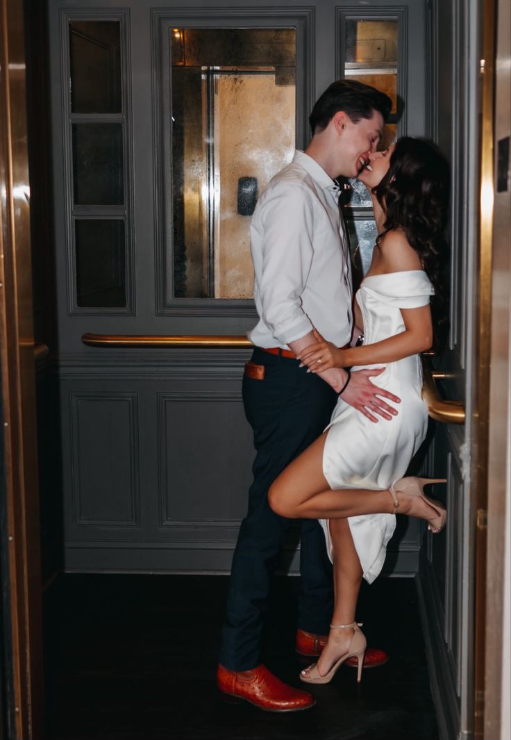 a man and woman kissing in front of an open door with red shoes on the floor